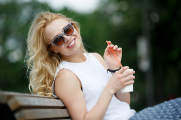 Blonde woman with milkshake wearing sunglasses in park