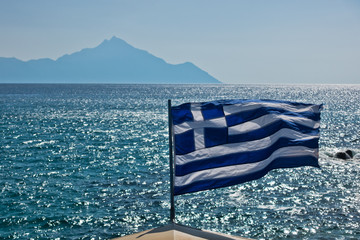 Greek flag on a sailing ship with holy mountain Athos in background, Greece