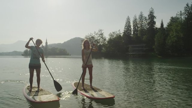 SLOW MOTION CLOSE UP: Girl friends oaring on stand up paddle boards