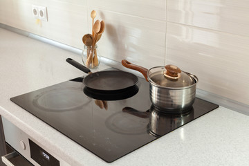 Open saucepan, pan and wooden spoons in modern kitchen with induction stove