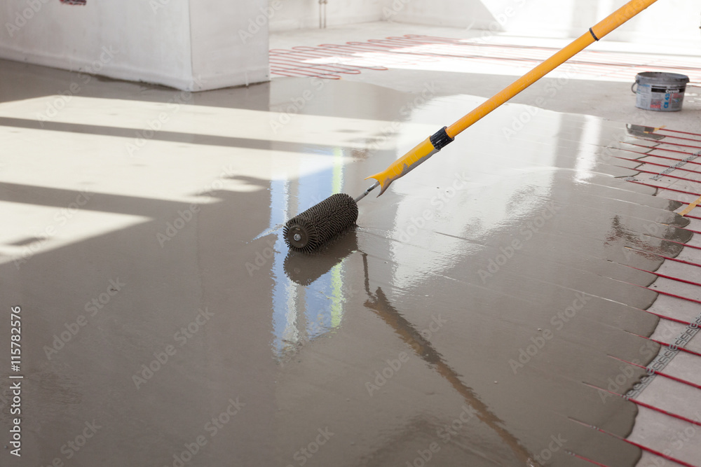 Wall mural Electric floor heating system installation in new house. Worker align cement with roller