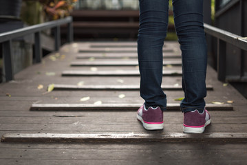 Fototapeta na wymiar women wearing jeans and sneakers step on old wooden bridge