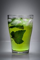 fresh cold drink with ice, mint leaves and black currant in glass on gray background