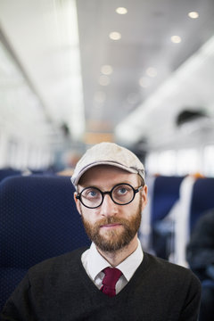 Man wearing flat cap and eyeglasses sitting in train