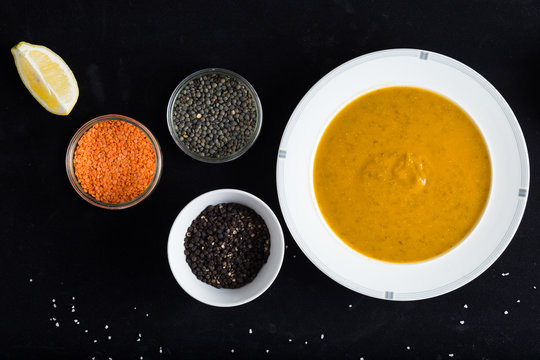 Cream soup of assorted lentil. Yellow and green lens, spices as raw for meal and lemon on black background. Healthy, appetizing, delicious, vegetarian food. Top view, copy space.
