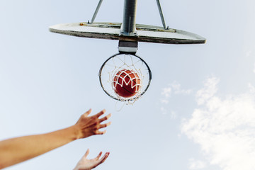 Cropped hands reaching basketball hoop against sky