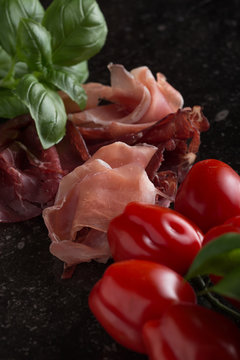 Jambon mix. Ham. Traditional Italian and Spanish salting, smoking, dry-cured dish - jamon Serrano and prosciutto crudo sliced with herbs and tomatos on dark stone background. Copy space. Closeup. 
