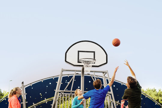 Low angle view of friends playing basketball at park against clear sky