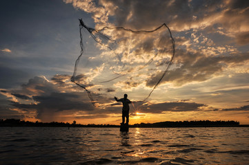A fisherman casting a net into the water during on  sunset
