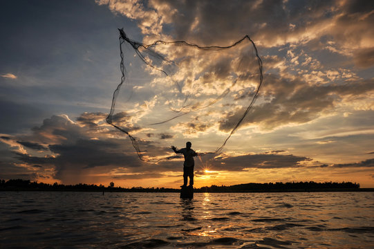 A fisherman casting a net into the water during on  sunset