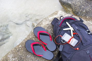 Sandals, luggage and smartphone on the  rocks at the seaside