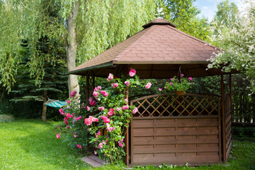 Outdoor wooden gazebo with roses and summer landscape background
