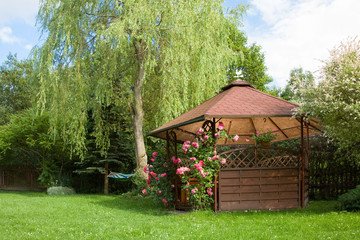 Outdoor wooden gazebo with roses and summer landscape background - obrazy, fototapety, plakaty