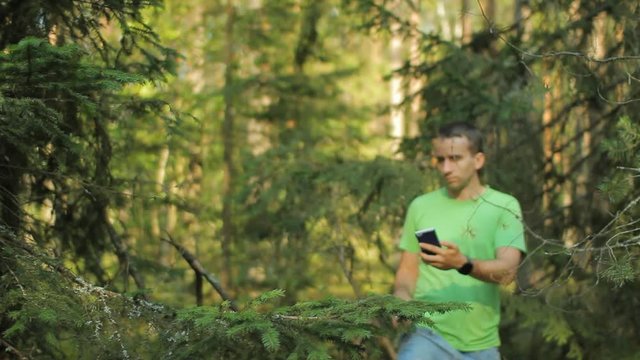 A man walks through the forest with the phone and looks at the navigation application. He chooses the right direction