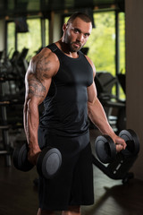 Fototapeta na wymiar Muscled Male Model Exercising Biceps With Dumbbells
