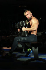 Fototapeta na wymiar Handsome muscular man sitting with dumbbells on dark background