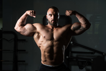 Fototapeta na wymiar Fitness Shaped Muscle Man Posing In Dark Gym