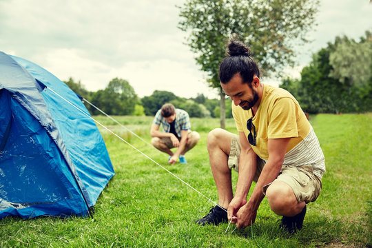 smiling friends setting up tent outdoors