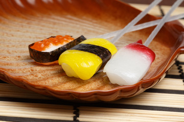 Beautiful colorful lollipops in the form of sushi lying on brown plate standing on striped bamboo mat.