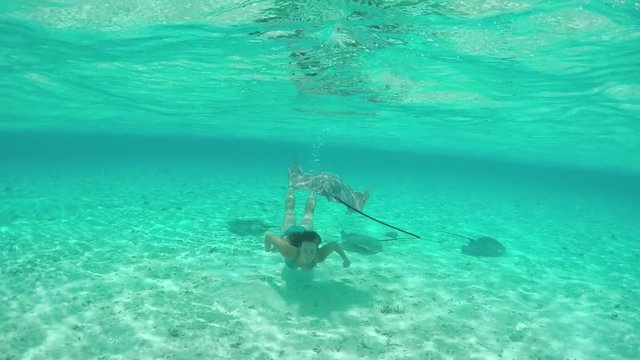 SLOW MOTION: Young woman swimming underwater with friendly stingray rays