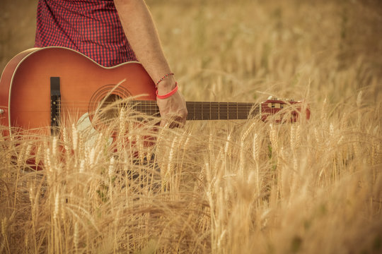 Close up of male holding guitar in wheat field. Music, instrument, and lifestyle concepts.