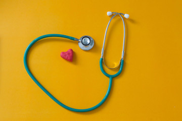Red heart and a stethoscope on yellow background