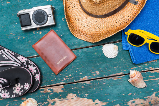 Strohhut, Flipflops, Reisepass, Fotoapperat und Muscheln auf Holzuntergrund