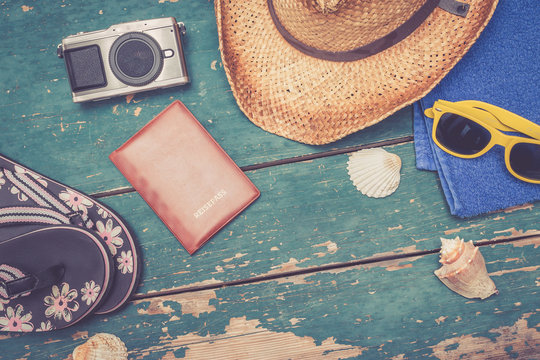 Strohhut, Flipflops, Reisepass, Fotoapperat und Muscheln auf Holzuntergrund, retro