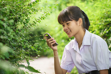 Smile teen thai student playing a smart phone in  the garden .