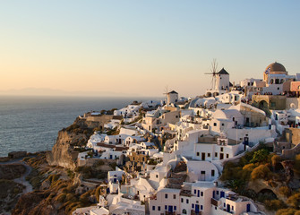 Fototapeta na wymiar Two white old mills on a background of white plastered houses at sunset in the town of Oia on Santorini island in Greece
