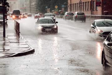 Moving car sprays puddle when heavy rain drops on concrete