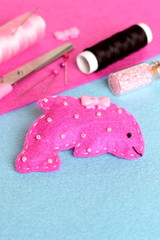 Pink felt dolphin toy on a blue background. Scissors, thread, needles, pins, beads, button. Funny sewing and craft activity for children. Stuffed sea animal toy pattern