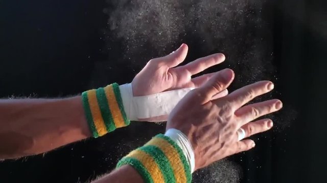 Taped hands of gymnast clapping white chalk powder into a slow motion cloud against dark background