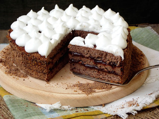 Truffle chocolate cake with prune jam covered with meringue on wooden platter