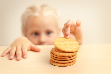 Funny little girl hiding behind white table and looking at pile of cookies