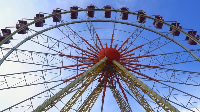 Bottom view on the Ferris wheel. Against the backdrop of a blue sky with clouds