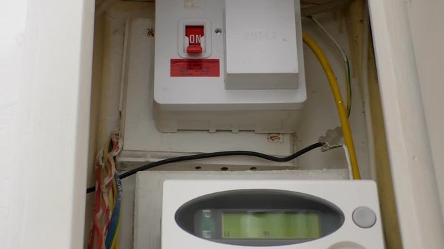 White domestic recessed electric meter box door opens showing main switch with fuses and top part of smart digital meter, the display readings