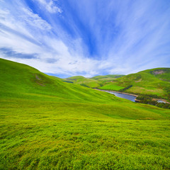 Landscape scenery of green Scottish valley with hills, river and cloudy blue sky