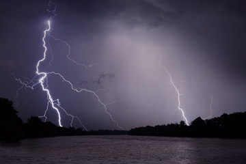 Thunder, lightnings and rain during storm over river and forest