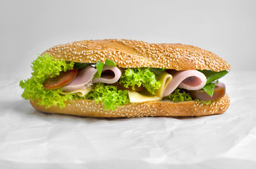 Big sandwich with ham and salad on a white parchment