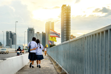 Selective focus on two schoolgirls , Flare light effect , Two asia schoolgirl walk across the bridge back home in the afternoon , Back view