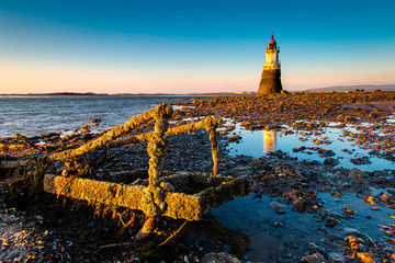 Plover Scar lighthouse at Cockerham on Morecambe Bay in the UK. The lighthouse has been damaged by the sea - the ladder in the foreground was once part of the structure. At sunset.