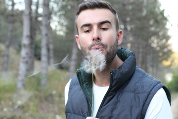 Guy blowing on white dandelion in the forest 