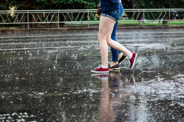 Two young women in boots crossing the street legs during heavy rain