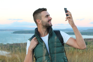 Just look! I am here! Handsome young man carrying backpack and taking a picture of himself and pointing to the gorgeous view