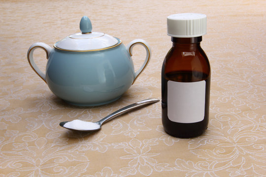 Medicine bottle with plain white label, sugar bowl, and a teaspoon of sugar