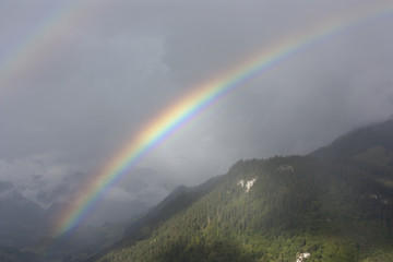 Double rainbow over misty forested hills in Switzerland.