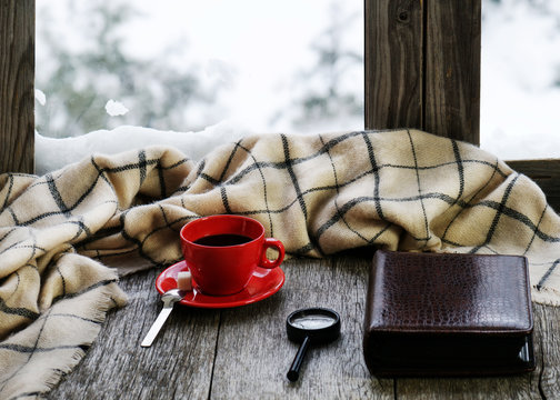 Red cup of coffee or tea on stylized wooden windowsill.