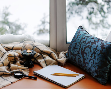Open notepad, magnifier glass, pillow, candle, pencils and plaid