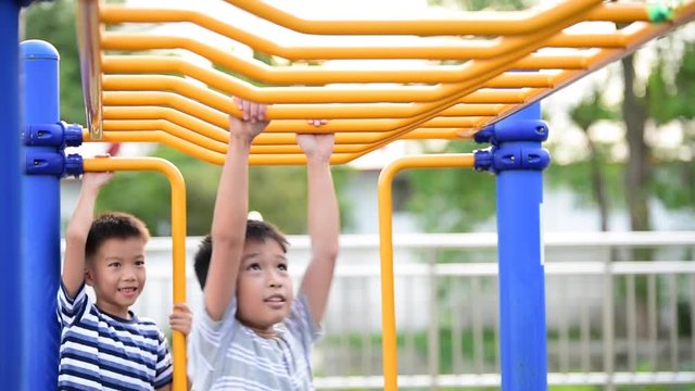 Two young asian boy hang the yellow bar by his hand to exercise at out door playground